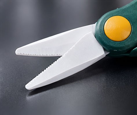 Close-up of the serrated zirconia ceramic blades on green-handled fishing scissors.